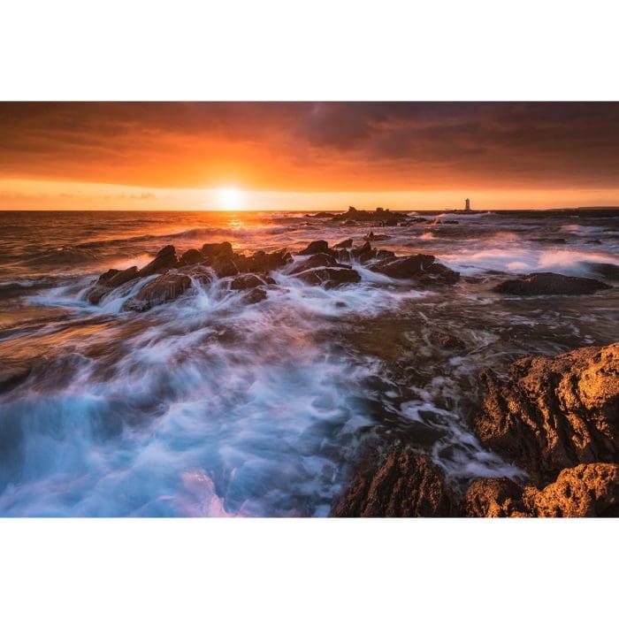 Onde sugli scogli al tramonto, con il faro di Mangiabarche sullo sfondo
