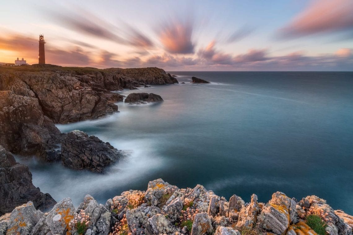 Faro sulla scogliera al tramonto, nuvole in scia